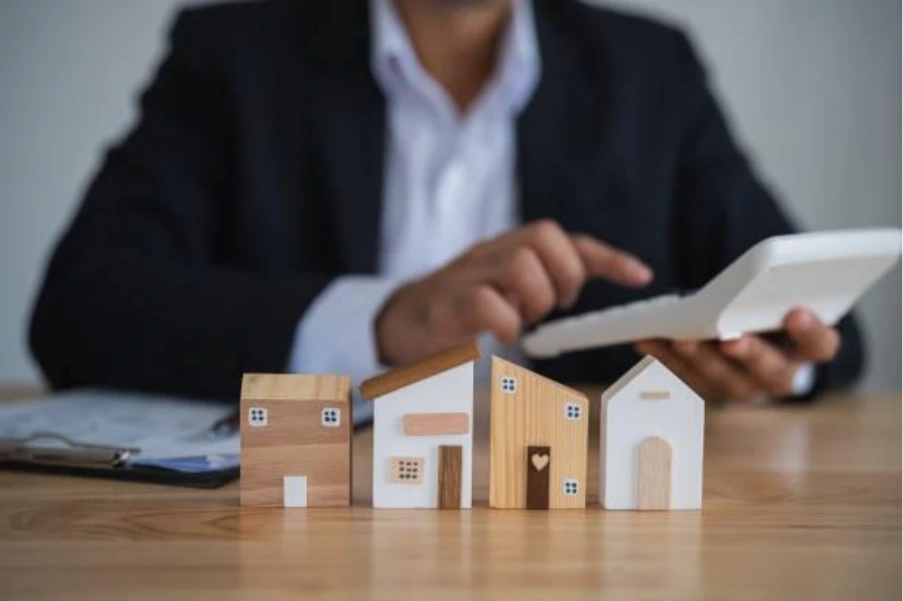 Wooden model houses on a desk with a property professional using a calculator, representing bridging finance for a UK chain break