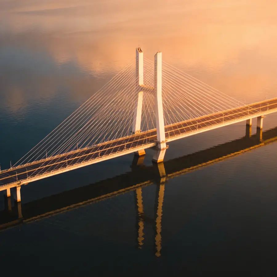 Aerial view of a suspension bridge over calm water at golden hour representing bridging finance in the UK