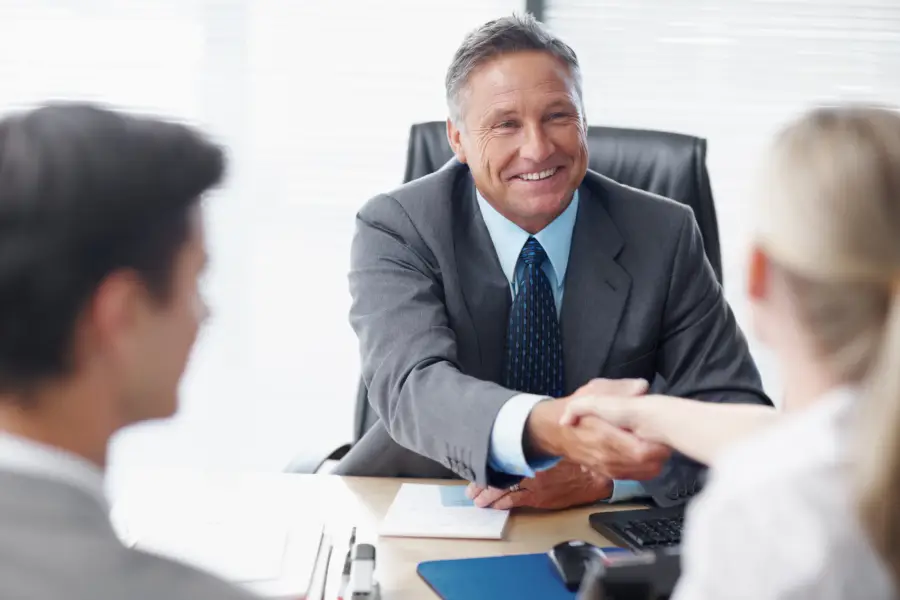 Commercial finance broker shaking hands with clients across a desk during a bridging loan consultation