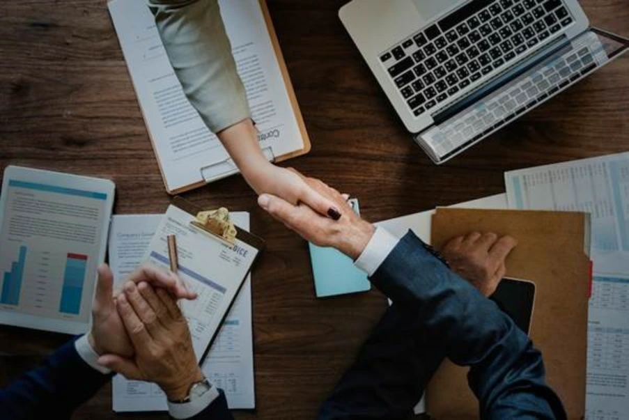 aerial view of two professionals shaking hands across desk with financial documents and charts representing successful completion of a UK commercial mortgage deal