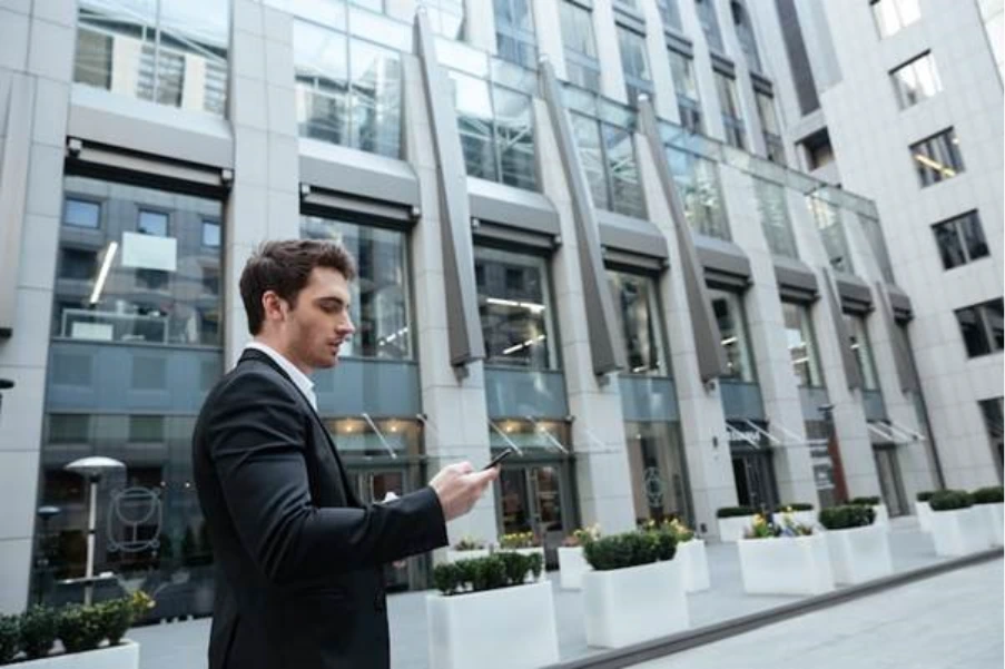 business professional checking phone outside modern commercial office building representing early stage of a UK commercial mortgage deal
