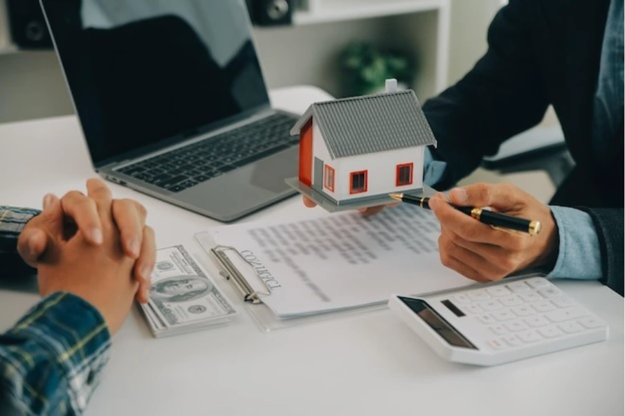 broker presenting house model to client across desk with loan documents and calculator representing bridging finance discussion for HMO conversion project