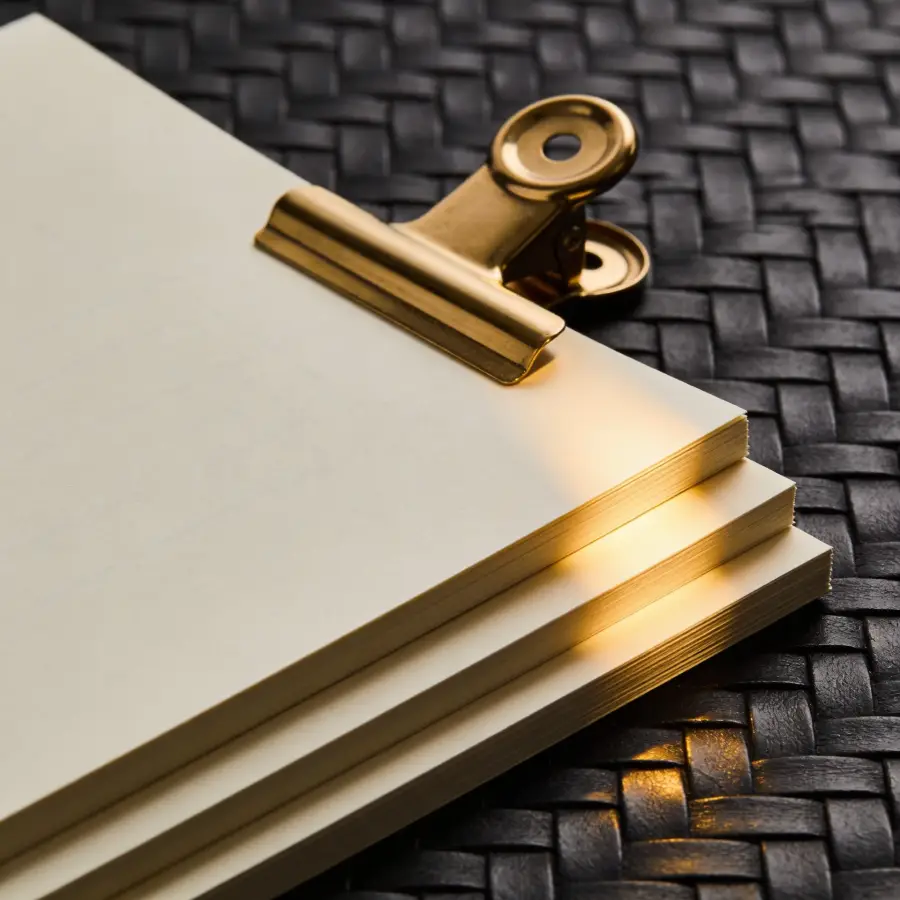 Stack of cream documents with brass clip on dark woven surface representing paperwork required for a UK bridging loan application