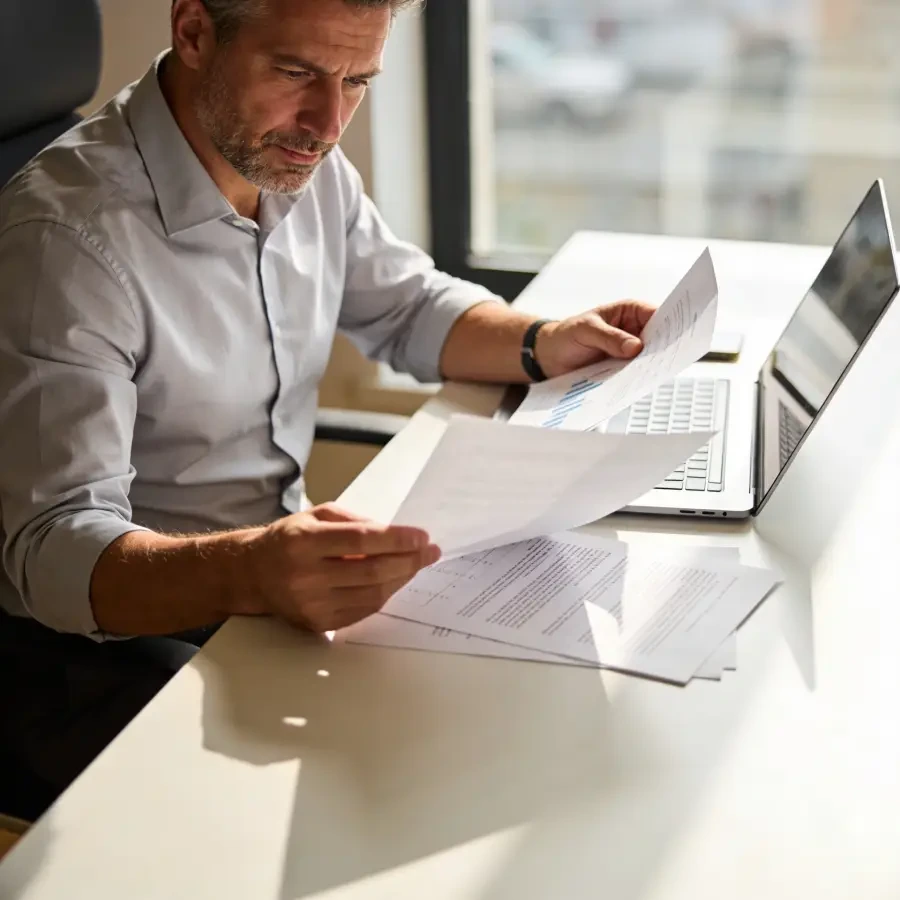Business owner reviewing company documents and accounts at desk with laptop