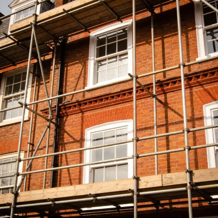 Red-brick UK period property undergoing refurbishment, scaffolding in place and freshly painted white sash windows